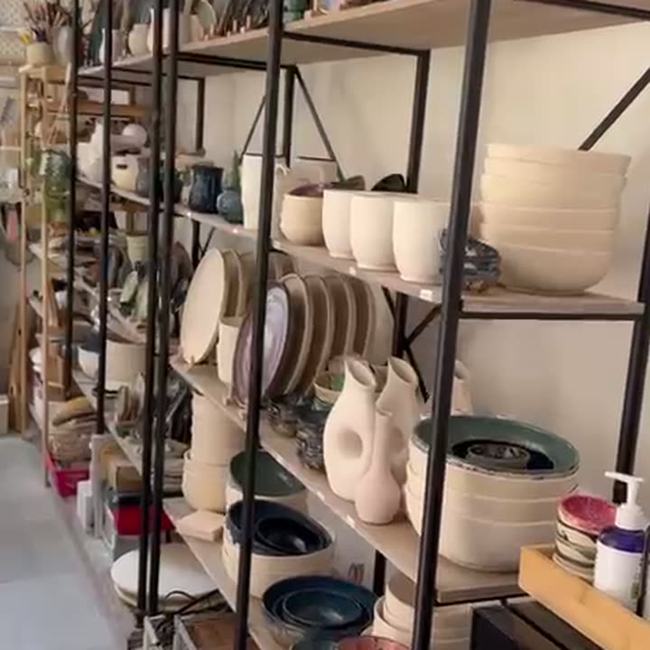 מדפי מתכת עמוסים בקערות, כדים וצלחות בגוונים בהירים